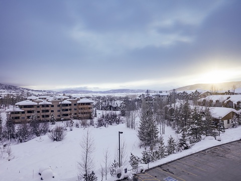 The property is situated in a serene winter mountain neighborhood blanketed in fresh snow, with distant peaks framing the peaceful residential area.