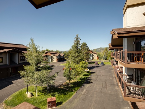 The property sits within a quiet mountainside community, featuring multi-level buildings, green lawns, mature trees, and ample parking in a serene natural setting.