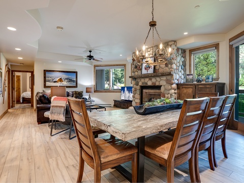 Gather around the stunning rustic dining table where natural light streams through garden views. The stone fireplace and open layout invite you to relax in comfort.