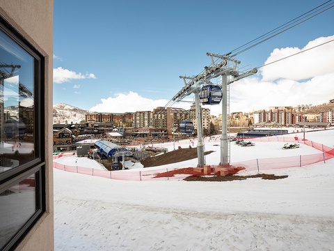 A mountain resort village features ski lifts, lodges, and snowy slopes beneath clear blue skies, set within a scenic alpine valley.