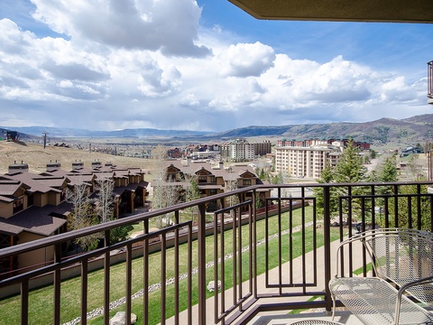 Scenic mountain resort area with rolling hills and dramatic cloud formations, photographed from a private balcony with outdoor seating.