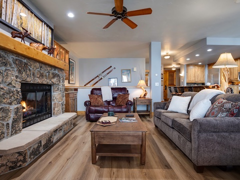Sink into plush seating by the crackling stone fireplace, where rustic elegance meets mountain comfort in your inviting living space.