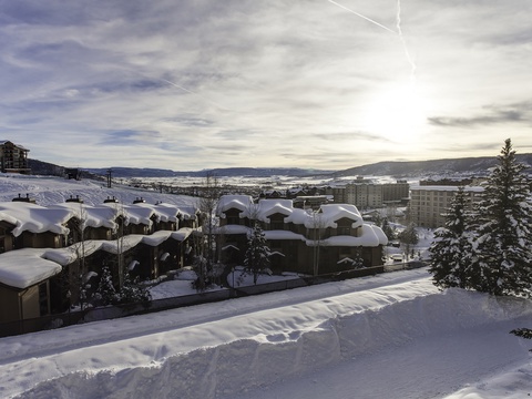 A scenic winter landscape showcasing a snow-covered mountain resort community nestled in rolling hills, with evergreen trees dotting the peaceful alpine surroundings.