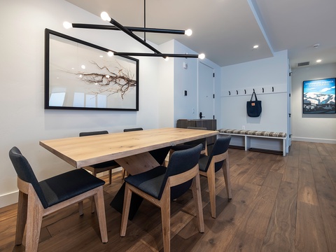 Gather around the stylish dining table under modern lighting, where warm wood tones and minimalist design invite you to share meals and create memories together.