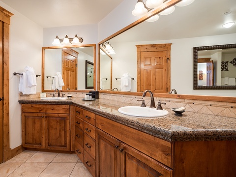 Your spacious bathroom features dual vanities with granite counters, warm wood cabinetry, and fresh white linens—perfect for unwinding after a day of adventure.
