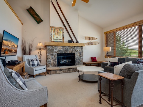 Gather in this inviting living room where a stone fireplace anchors the space, plush seating surrounds the coffee table, and mountain views frame your cozy alpine retreat.