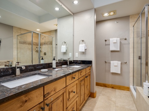 Unwind in your beautifully appointed bathroom featuring dual vanities, a spacious walk-in shower, and warm wood cabinetry. Fresh towels and modern fixtures await your arrival.