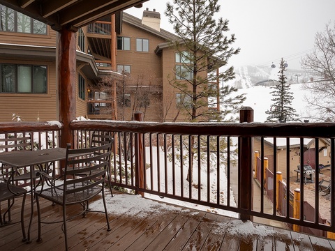 A covered balcony overlooks a snowy ski resort area with slopes and lifts visible beyond the surrounding lodges and pine trees.