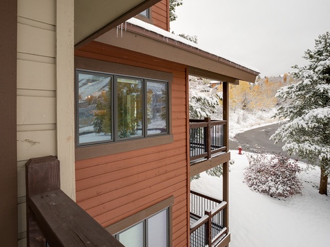 A snow-covered mountain landscape surrounds the property, with pine trees and distant slopes creating a peaceful winter setting beyond the balcony.