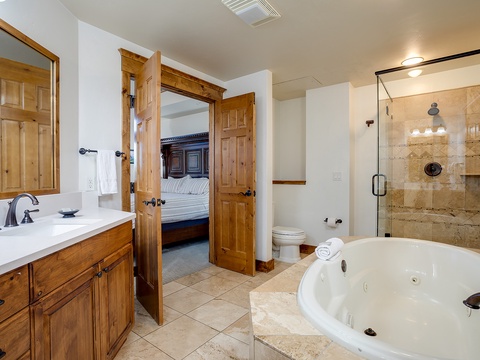 Your private ensuite features a jetted soaking tub, walk-in shower with built-in niche, and rustic wood details that blend luxury with mountain charm.