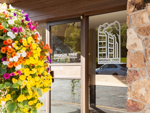Colorful blooms greet you at the entrance, framing the property's welcoming glass doors and stone facade. A bright, cheerful arrival awaits your vacation stay.