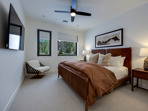 Unwind in your serene bedroom with a plush bed, modern ceiling fan, and peaceful views of the surrounding greenery through large windows.