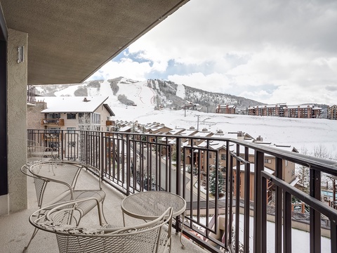 Expansive balcony overlooking snow-covered ski slopes and surrounding village, framed by mountain views. A perfect spot to watch winter adventures unfold below.
