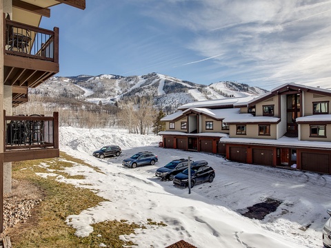Mountain resort property nestled at the base of ski slopes, featuring convenient parking and alpine views of the surrounding winter landscape.