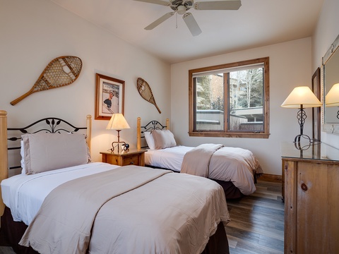 Drift off in this cozy alpine bedroom with two plush twin beds, rustic wood furnishings, and charming snowshoe accents. Wake to soft natural light and peaceful mountain views from your window.