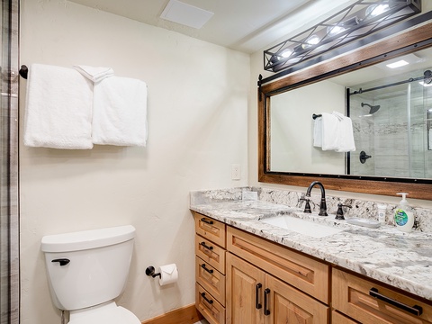 Your private bathroom features a spacious marble vanity, elegant wood cabinetry, and a sparkling glass-enclosed shower—perfect for unwinding after a day of adventure.