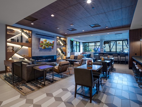 Modern communal lounge with sleek seating, a glowing fireplace, bar area, and bright windows offering scenic views—ideal for gathering and unwinding.