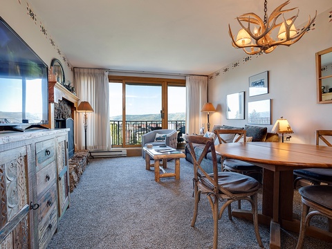 Cozy mountain-inspired space with antler chandelier, rustic furnishings, and expansive windows framing stunning views—perfect for relaxing after a day of adventure.