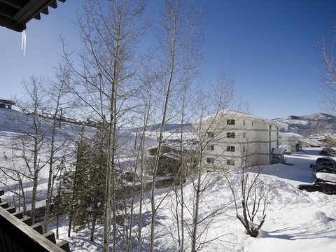 A winter mountain setting with snow-covered slopes and bare trees under clear blue skies, offering a peaceful ski resort atmosphere.