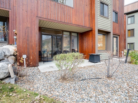 Modern mountain condo featuring warm wood siding, private patio, and natural landscaping in a peaceful mountain community setting.