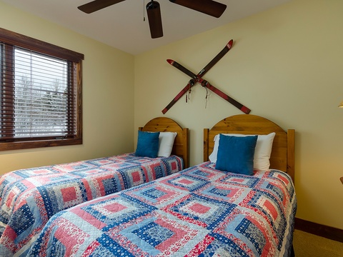 Settle into your cozy room with comfortable twin beds dressed in cheerful quilts, a ceiling fan overhead, and natural light streaming through wood-framed windows to welcome you after your alpine adventures.