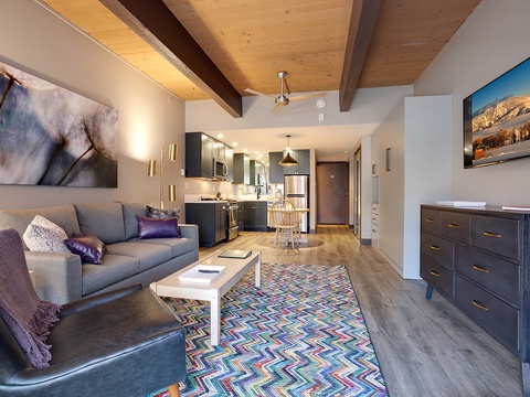 Relax in your bright, open living space featuring warm wood-beam ceilings, a cozy seating area, and a fully-equipped kitchen, all within easy reach for your mountain getaway.