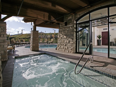 The property features indoor/outdoor hot tubs with scenic mountain views. Multiple spa areas provide relaxation options beneath natural stone columns and covered decks.