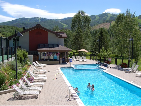 Mountain resort pool area surrounded by lush greenery and scenic peaks, offering relaxation and recreational swimming in a beautiful alpine setting.
