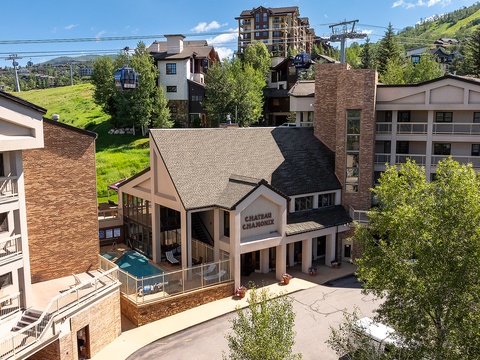 Mountain resort property in a year-round recreation area, with ski lifts and green slopes visible in the surrounding landscape. Summer-season exterior view of the building and its location.