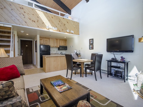 Your open-concept retreat features soaring vaulted ceilings and a cozy loft above, bathed in natural light from oversized windows. Warm wood tones and a stone fireplace create instant mountain charm.