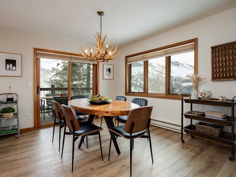 Gather around the handcrafted wood table for meals with unforgettable mountain views through expansive windows. The rustic antler chandelier adds warmth, and the deck beyond invites you to enjoy your morning coffee outdoors.