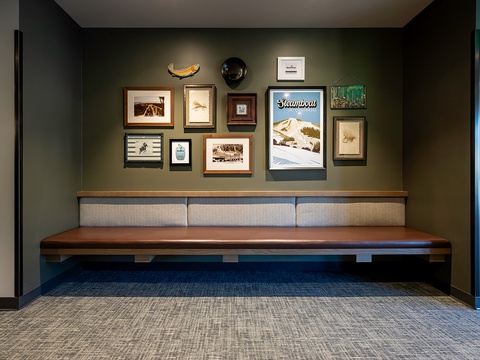 Styled seating area features curated wall art celebrating local mountain culture and outdoor adventure, with a warm wooden bench providing a cozy spot to relax.