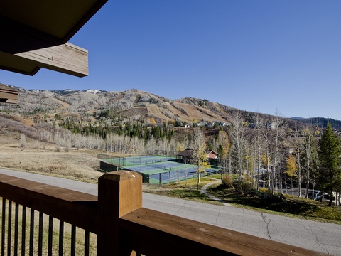 A mountain resort property featuring tennis courts, ski slopes, and natural forested surroundings under clear blue skies.