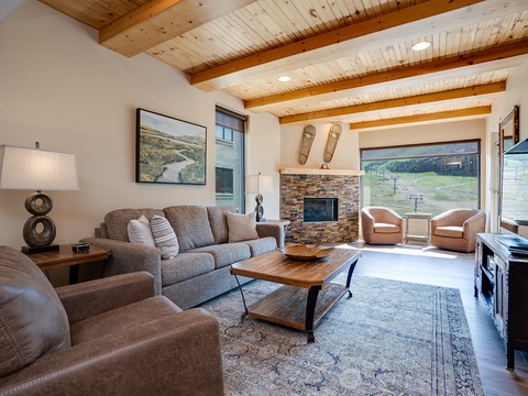Step into your cozy living room with vaulted wood-beam ceilings, a stone fireplace, and sweeping mountain views—your perfect retreat after a day of adventure.