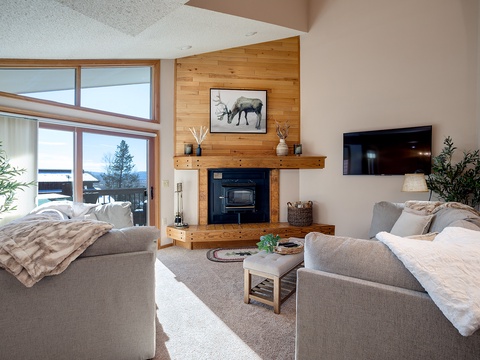 Unwind in your bright living room with plush sofas, a warm fireplace, and serene lake views through soaring windows—your perfect mountain retreat for cozy evenings together.