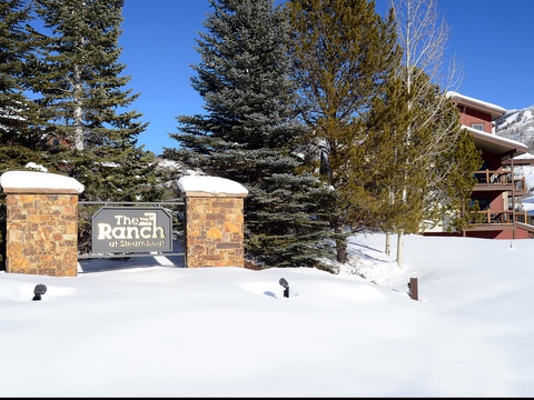 The Ranch at Steamboat entrance welcomes visitors with stone pillars and signage, surrounded by snow-dusted evergreens and mountain views in a picturesque alpine setting.