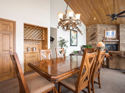 Picture yourself sharing meals around this beautiful wooden dining table beneath rustic chandeliers, with the cozy living room and fireplace just steps away for post-dinner relaxation.