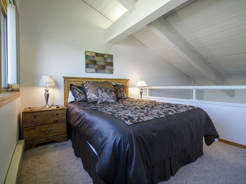Your cozy loft bedroom awaits with vaulted ceilings, natural light, and a comfortable bed dressed in elegant linens—perfect for peaceful rest after a day of adventure.