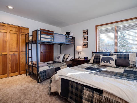 Unwind in your cozy mountain-themed bedroom featuring a plush queen bed and fun bunk beds, perfect for family bonding. Natural light streams through the large window, illuminating snowy pines outside.