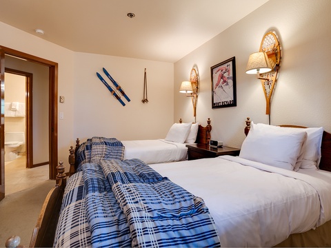 Unwind in your cozy twin bedroom with plaid accents and vintage ski lodge charm. Soft lighting and unique snowshoe sconces set a warm, inviting mountain mood.