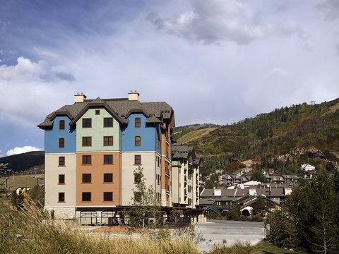 A distinctive mountain resort building with colorful pastel facades set against forested alpine slopes and a dramatic sky.
