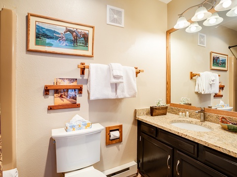 Your private bathroom features elegant granite countertops, fresh towels, and thoughtful touches like artwork and wooden accents creating a warm, inviting retreat.