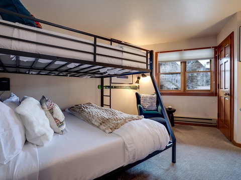Cozy bunk room with a full bed below and twin above. Natural light pours in from the window, perfect for your group or family's mountain retreat.