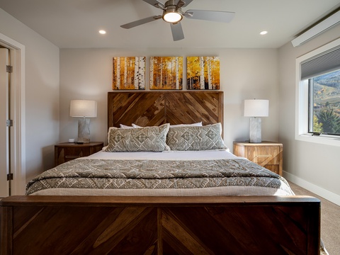 Drift off in this serene bedroom with a plush bed, warm wood accents, soft lighting, and stunning views framed by the window—your restful retreat awaits.
