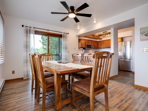 Gather around this inviting dining table for meals and memories. Natural light streams through the windows, while the open layout connects you to the fully-equipped kitchen—perfect for your mountain getaway.
