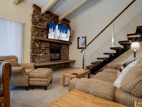 Curl up on plush sofas by the stone fireplace, where alpine art and exposed beams create a cozy mountain retreat. Modern floating stairs and soft lighting make your alpine getaway feel warm and inviting.