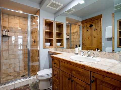 Your private bathroom features a spacious walk-in shower with elegant tile work, warm wood cabinetry, and thoughtful amenities to make your stay comfortable.