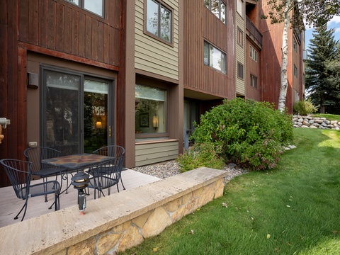 Multi-unit vacation rental building featuring private patio areas with outdoor dining, lush green lawns, and mature landscaping in a peaceful mountain setting.