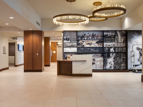 The hotel lobby welcomes arrivals with elegant circular chandeliers, polished tile floors, and striking wall art showcasing outdoor adventure scenes, setting a sophisticated yet inviting tone.