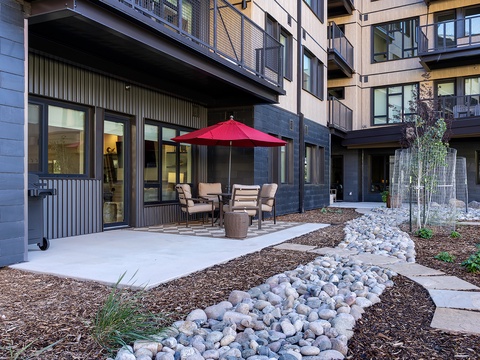 A modern multi-level residential complex featuring contemporary architecture with natural landscaping, stone pathways, and ground-floor patio areas designed for relaxation.
